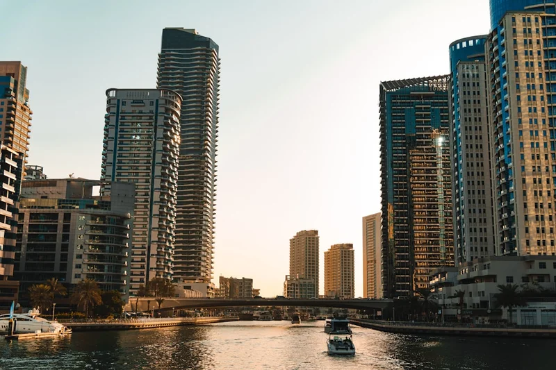 Modern skyscrapers line a calm canal with boats.